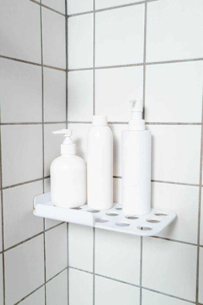 Stylish bathroom corner with minimalist white bottles on a shelf, emphasizing simplicity.